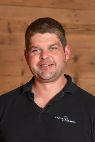 Mitarbeiterportrait / Foto mit braunem T-Shirt oder schwarzem Polo Shirt mit Zimmerei Hirschi Logo. Strahlend und lachend nach oben schauend oder direkt in die Kamera.