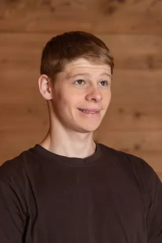 Mitarbeiterportrait / Foto mit braunem T-Shirt oder schwarzem Polo Shirt mit Zimmerei Hirschi Logo. Strahlend und lachend nach oben schauend oder direkt in die Kamera.