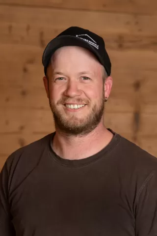 Mitarbeiterportrait / Foto mit braunem T-Shirt oder schwarzem Polo Shirt mit Zimmerei Hirschi Logo. Strahlend und lachend nach oben schauend oder direkt in die Kamera.