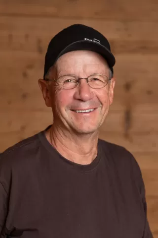 Mitarbeiterportrait / Foto mit braunem T-Shirt oder schwarzem Polo Shirt mit Zimmerei Hirschi Logo. Strahlend und lachend nach oben schauend oder direkt in die Kamera.