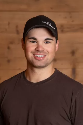 Mitarbeiterportrait / Foto mit braunem T-Shirt oder schwarzem Polo Shirt mit Zimmerei Hirschi Logo. Strahlend und lachend nach oben schauend oder direkt in die Kamera.