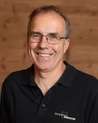 Mitarbeiterportrait / Foto mit braunem T-Shirt oder schwarzem Polo Shirt mit Zimmerei Hirschi Logo. Strahlend und lachend nach oben schauend oder direkt in die Kamera.