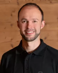 Auf diesem Foto ist ein neuer Mitarbeiter der Zimmerei Hirschi AG zu sehen. Er steht vor einer alten Holzwand in einem der wunderschönen Büroräume im Längengrund, Trub. Er trägt ein braunes beschriftetes Zimmerei Hirschi T-Shirt, einen Zimmerei Hirschi Hut. Als Zimmermann stossen die neuen Mitarbieter in ein flexibles, angenhemes, lustiges, inovatives, zukunftsorientieres, aufgeschlossenes Team. Wir wünschen im alles Gute.