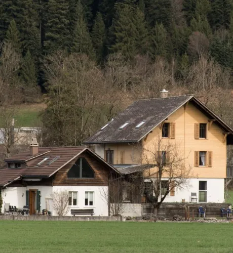 Referenzprojekt der Zimmerei Hirschi AG: Wohnhaus mit umfassend erneuerter Holzfassade, eingebettet in die typische Landschaft des Emmentals mit Wiesen und bewaldetem Hang.