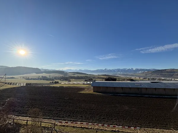 Holzhaus im Bau mit eingerüsteter Fassade und Baustellenbanner der Zimmerei Hirschi unter blauem Himmel.